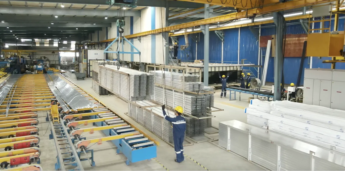Overhead crane moving a load of sections between stations, seen from above