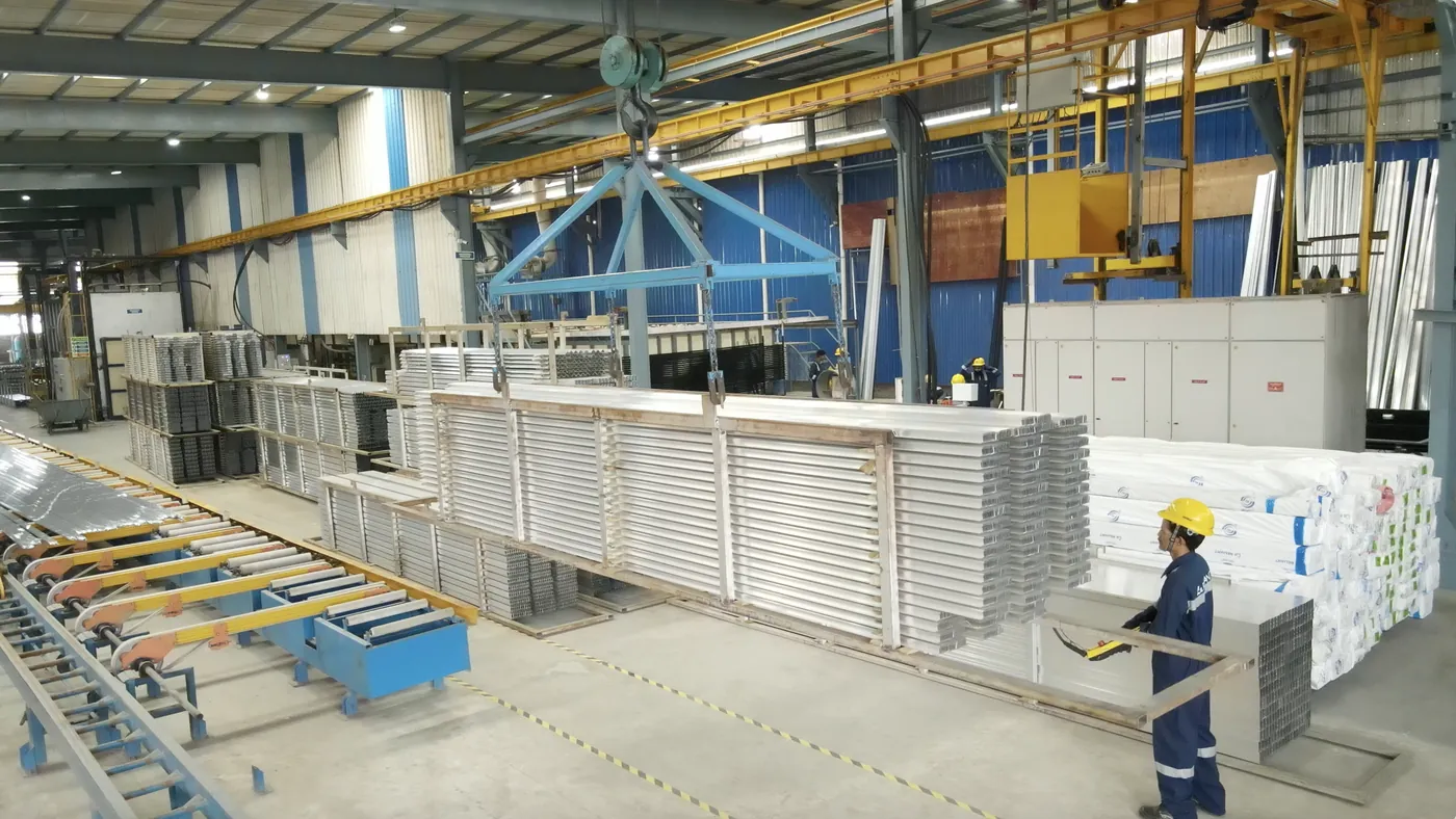 Overhead crane lifting a load of aluminium sections, with an operator at the controls