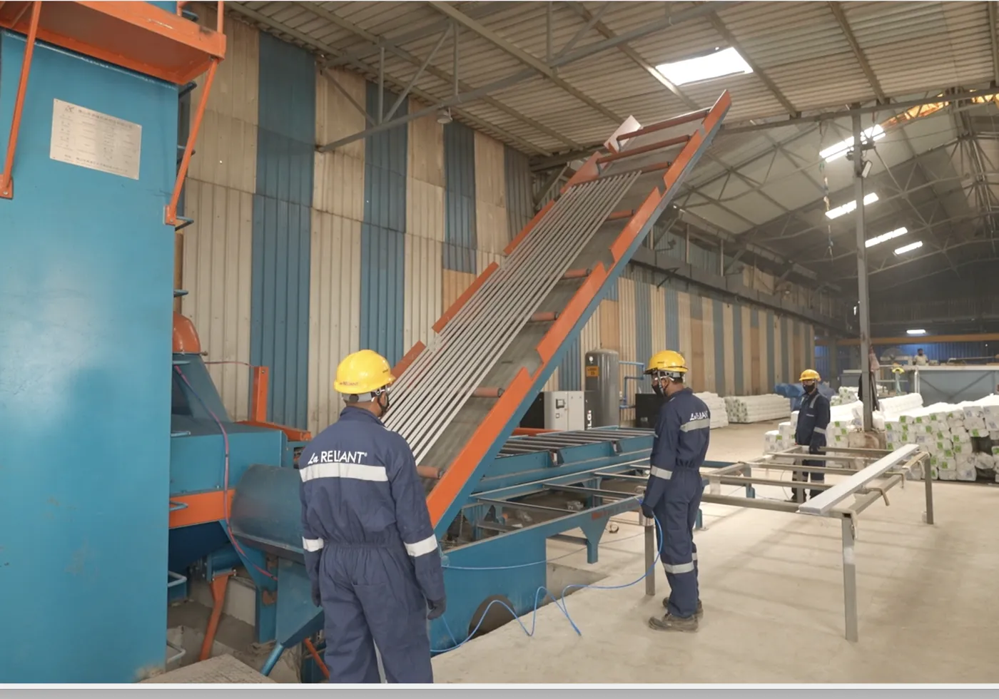 Operators loading aluminium profiles onto the shot blasting conveyor